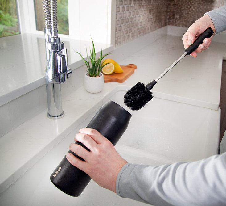 Person cleaning a bottle with a specialized bottle brush